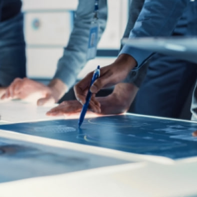 Colleagues marking up a blueprint with a pen on a light table.